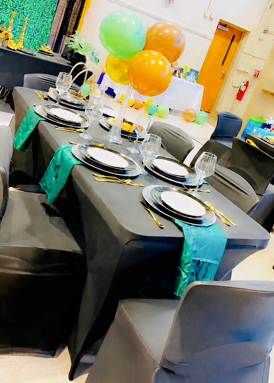 Safari-themed baby shower tablescape with black linens, jewel-tone balloons, gold chargers, and tropical greenery